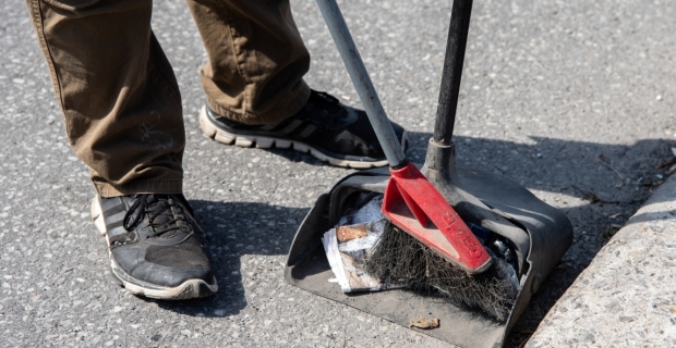 Un travailleur poussant des détritus se trouvant dans la rue dans une pelle à poussière, à l'aide d'un balai