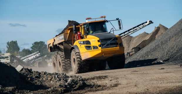 Un gros camion à benne rempli de terre traverse des piles de sable trié