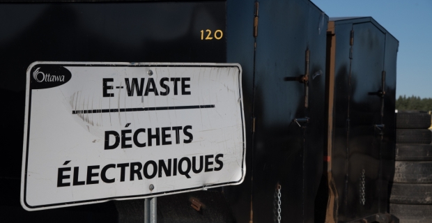 A sign that says "E-Waste" in front of large black containers